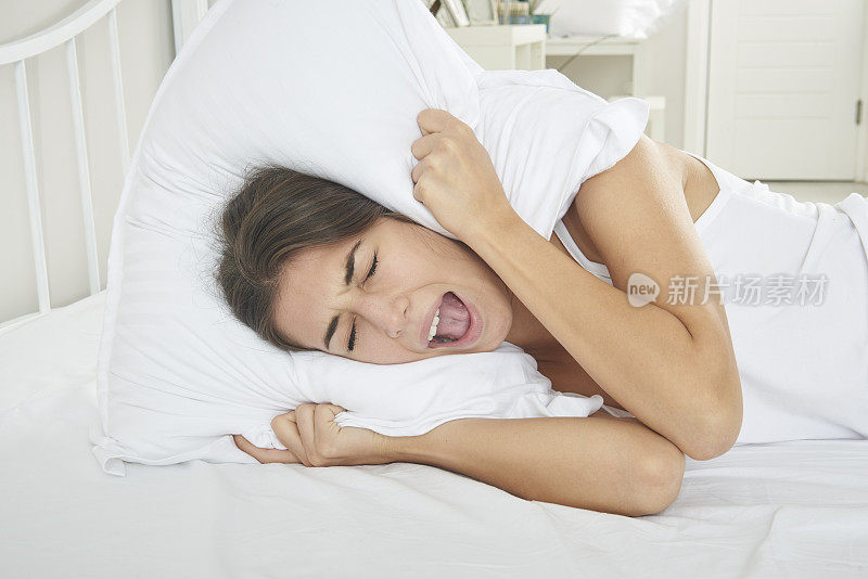 一个躺在床上用枕头捂住耳朵的女人