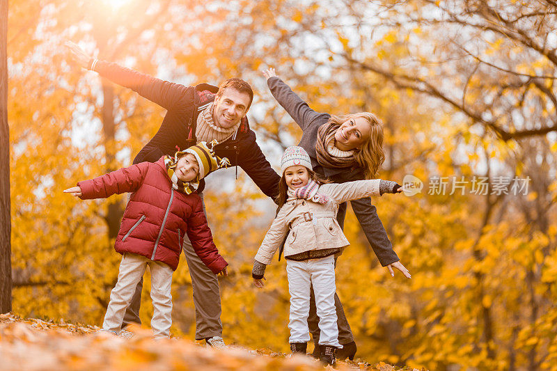 顽皮的一家人伸开双臂站在秋天的公园里。
