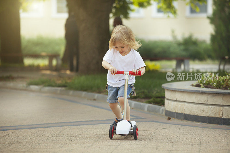 一个金发小男孩在公园里骑滑板车