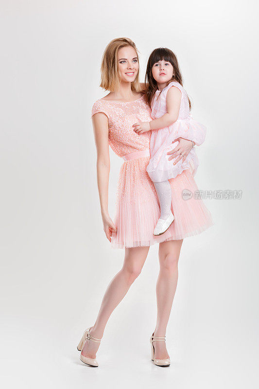 金发妈妈抱着可爱的小女儿在粉红色的公主裙