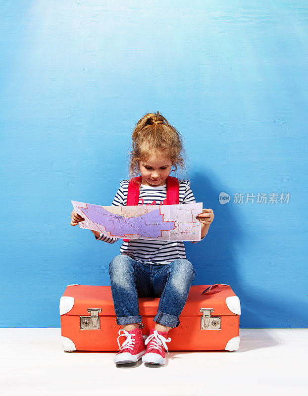 金发碧眼的小女孩带着粉色的复古行李箱和城市地图准备迎接暑假。旅行和冒险概念