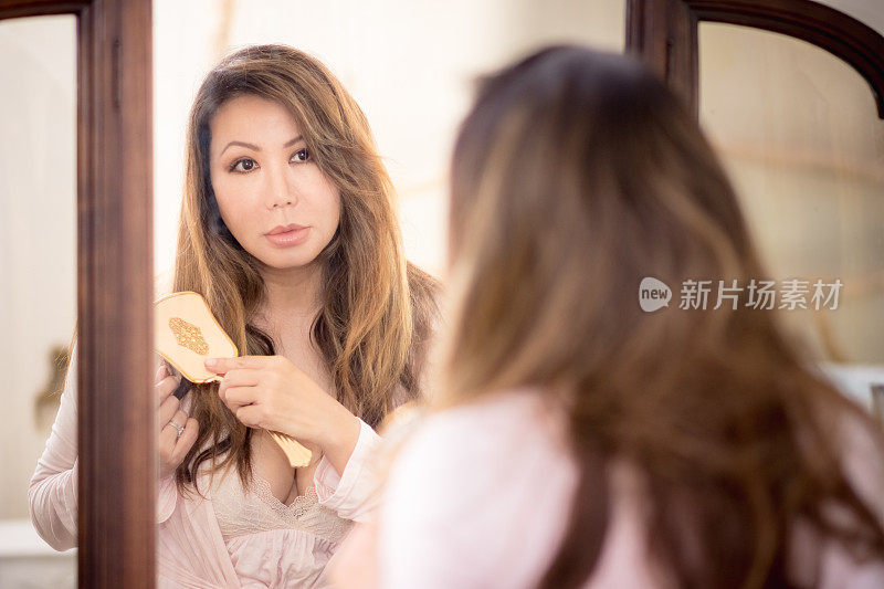 美丽的亚洲女人看着复古镜梳头发