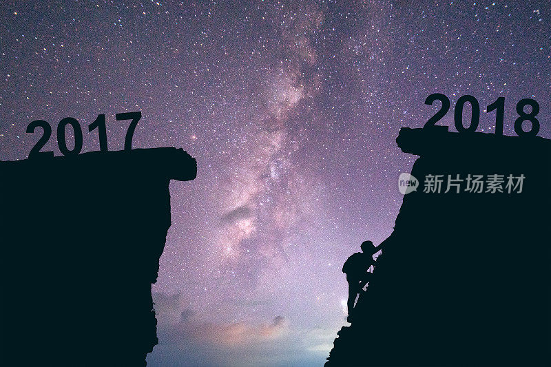 2017年至2018年间，年轻人在攀登。新年快乐2018概念银河系背景