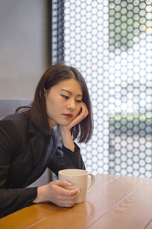 一个沉思的女人在咖啡馆拿着一杯咖啡的肖像