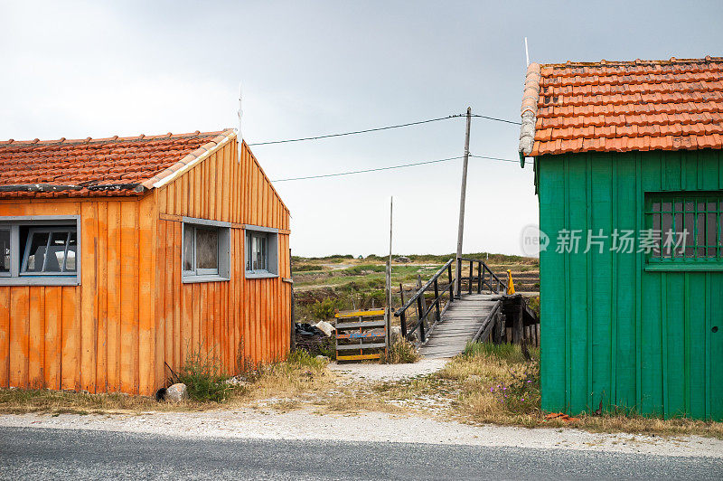 在法国奥勒隆岛上，暴风雨般的灰色天空下，五颜六色的牡蛎棚和一个木制的临时人行桥