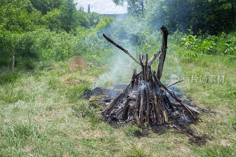 在夏天的森林里，一堆熊熊燃烧的大火和一只萨满手鼓就在附近。
