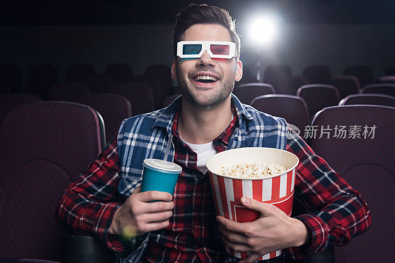 一个戴着3d眼镜、喝着苏打水吃着爆米花的兴奋男人正在电影院看电影