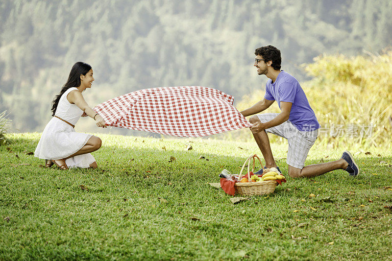西班牙年轻夫妇在草地上设置野餐毯子