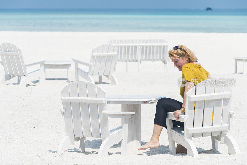 美丽的，资深的女人坐在椅子上，享受小岛屿海滩在四月，马尔代夫