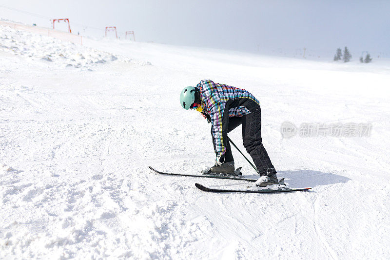 一名女子滑雪者在雪坡上清理雪地上的滑雪靴