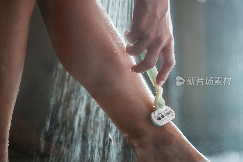 一个女人剃她的腿在淋浴下的特写。