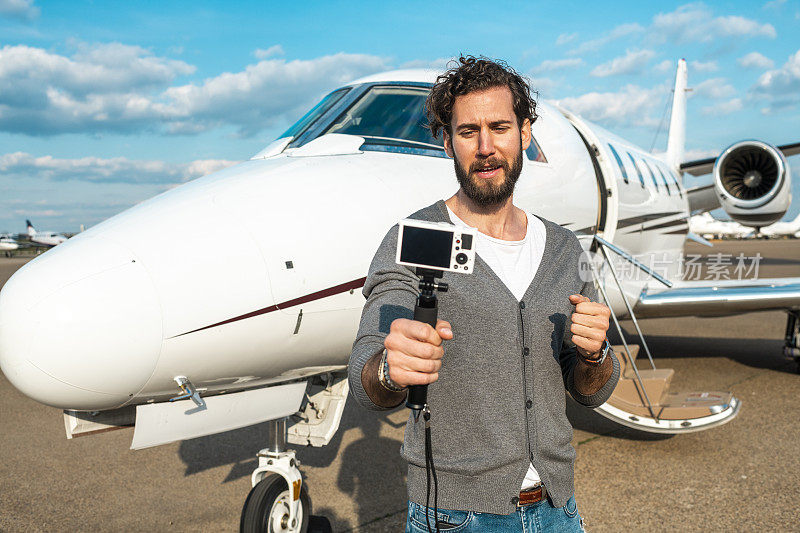 著名的社交媒体名人和视频博主正在用一个小摄像机拍摄一架停在机场滑行道上的私人飞机的头锥