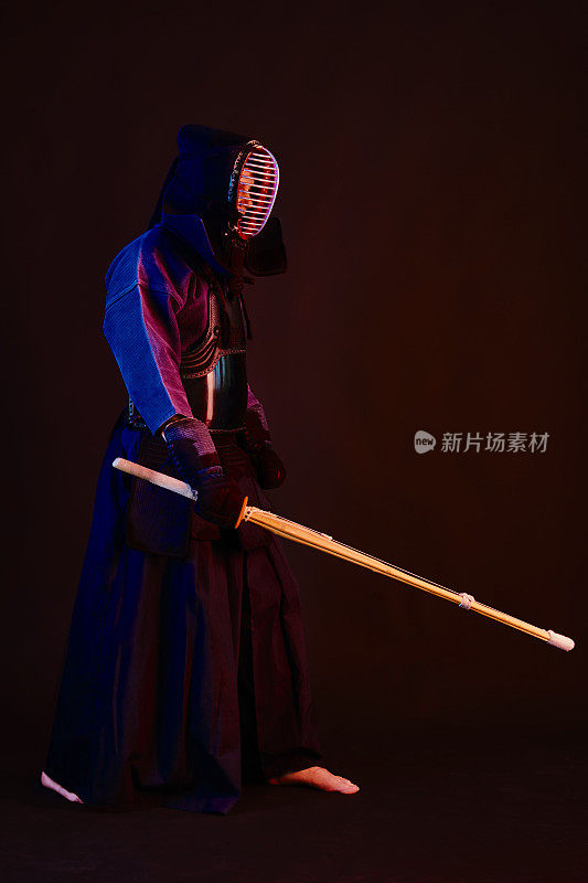 近景，剑道战士穿着盔甲，传统和服，头盔练习武术与shinai竹剑，黑色背景