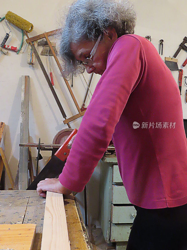 老妇人正在用手锯锯一块木板