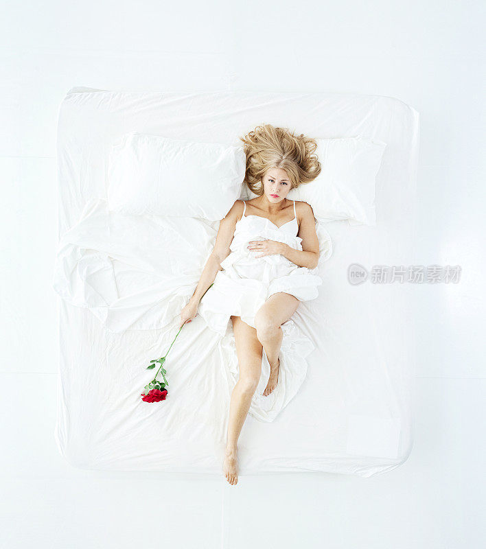 年轻的白人妇女在卧室的白色背景前放松，穿着内衣，拿着玫瑰花