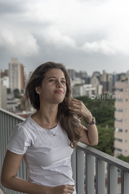 一个自信的年轻巴西女人，站在阳台上，看着窗外的景色，思考着未来