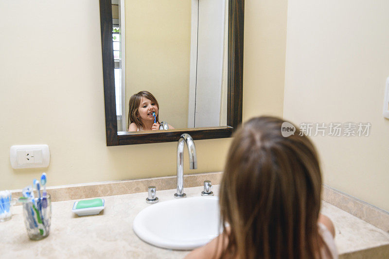 微笑的小女孩一边刷牙一边对着镜子