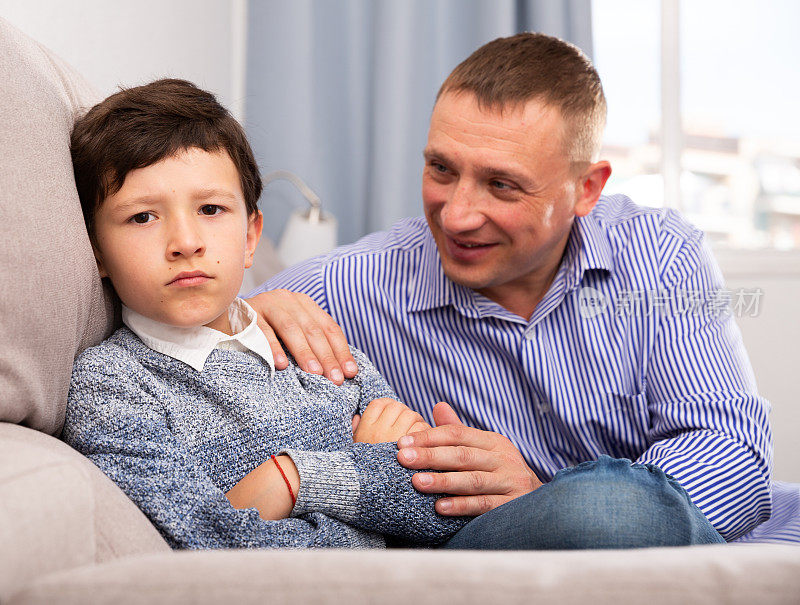 争吵后，年轻的父亲安慰坐在沙发上的儿子
