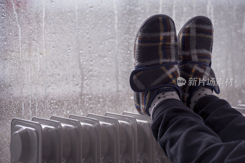 孩子的脚上穿拖鞋，在雨季冬天用油加热器暖脚。