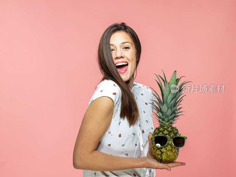 顽皮的年轻女子拿着菠萝在珊瑚的背景