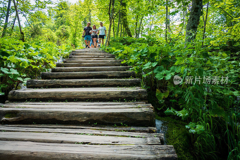 克罗地亚Plitvice湖国家公园，年轻人在小而隐蔽的瀑布上方的木板路上散步