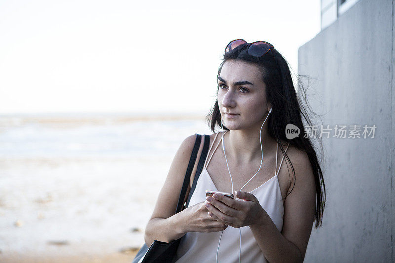 一个少女在夏天靠在墙上用智能手机，背景是大海