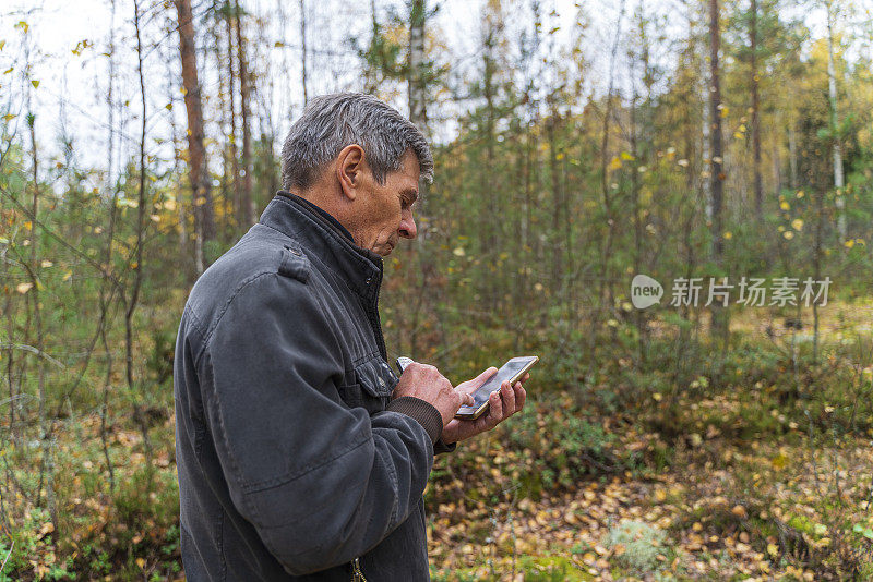 一个老人在森林里用智能手机上安装的移动应用程序查看方向。