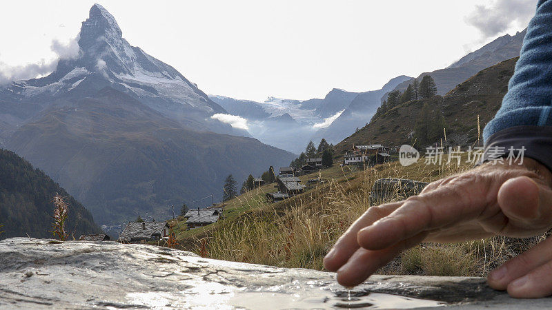 一名男性徒步旅行者停下脚步，用手指触摸潮湿的岩石