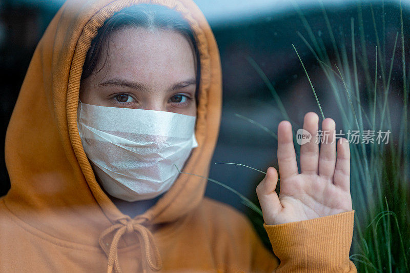 一个戴着外科口罩的少女站在窗前看