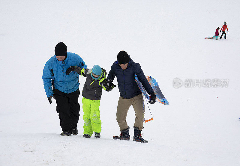 两名男子帮助小孩爬上雪橇山