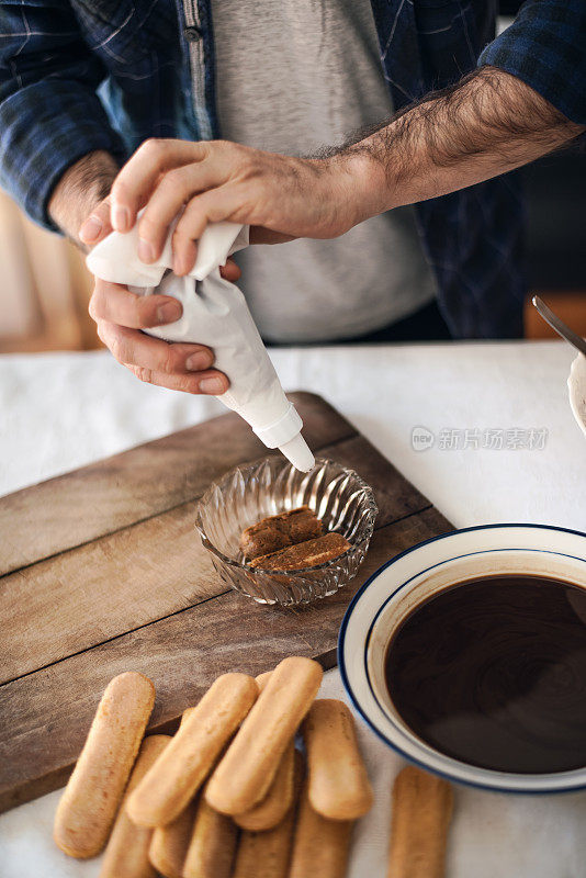 隔离烹饪:一名男子正在用糖衣袋给提拉米苏填馅