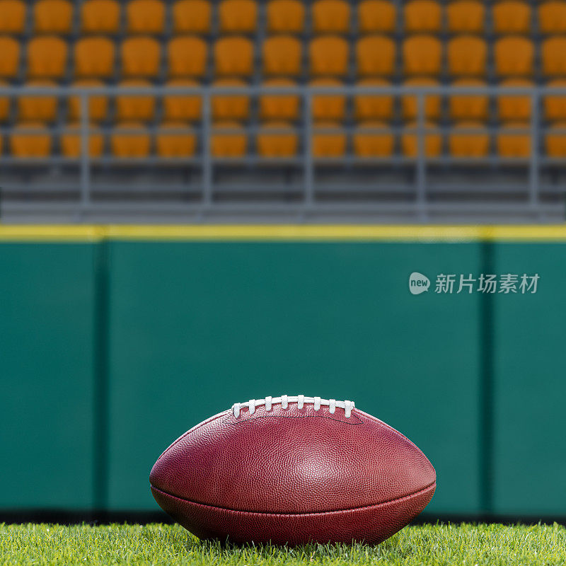 草地上放着一个美式足球，背景是橙色的空座位
