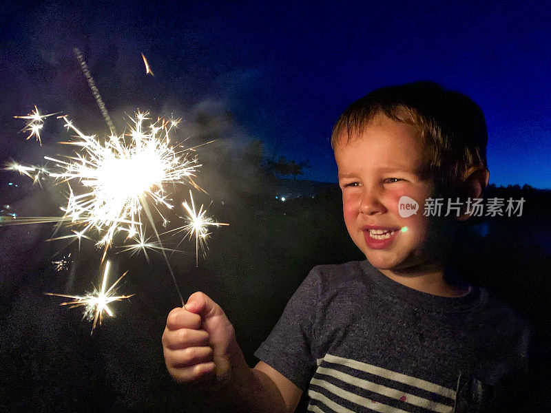 一个可爱的，四岁的白人男孩微笑着看着明亮的烟花在7月4日