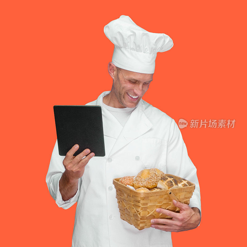 白人年轻男性面包师在橙色的背景，穿着裤子，拿着法棍，使用触摸屏