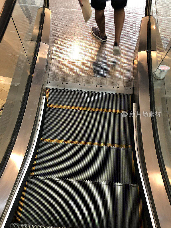 一个不认识的人在喷涂着白色大蜱的自动扶梯上使用金属台阶的图像，关于移动楼梯台阶的冠状病毒社交距离规定，新冠病毒安全