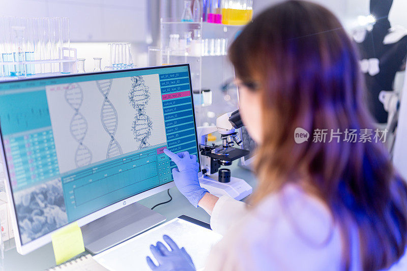 在电脑键盘上打字的女科学家。以DNA研究为背景的监视器