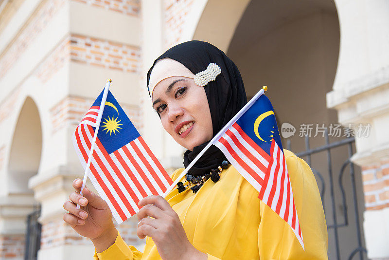 年轻的马来西亚妇女挥舞着马来西亚国旗，带着高昂的爱国主义精神庆祝独立日