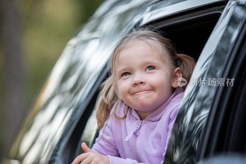 在停车场里，快乐的小女孩探出车窗，对她所看到的微笑