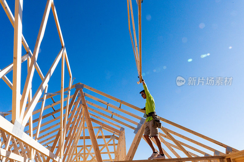 一个构架师站在一个新房屋建筑的骨架墙上，指导起重机操作员安装另一个桁架