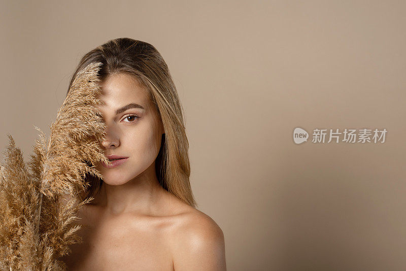 可爱的年轻女模特，松散的头发握着干燥的潘帕斯草在她的手中。从小麦谷物中提取天然化妆品的概念。皮肤护理