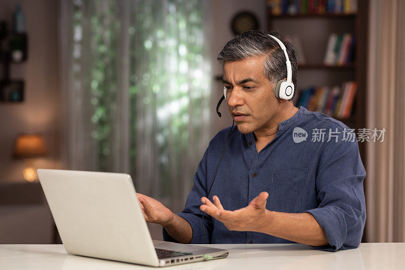 拍摄一个成熟的商人在家里使用笔记本电脑和耳机:股票照片