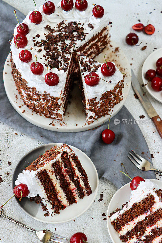 蛋糕架上的黑森林蛋糕图片，上面有玫瑰形的奶油蛋糕，上面有樱桃，奢华的巧克力蛋糕上点缀着奶油，上面覆盖着巧克力屑，灰色的薄纱，刀，大理石效果的背景，高架的视野
