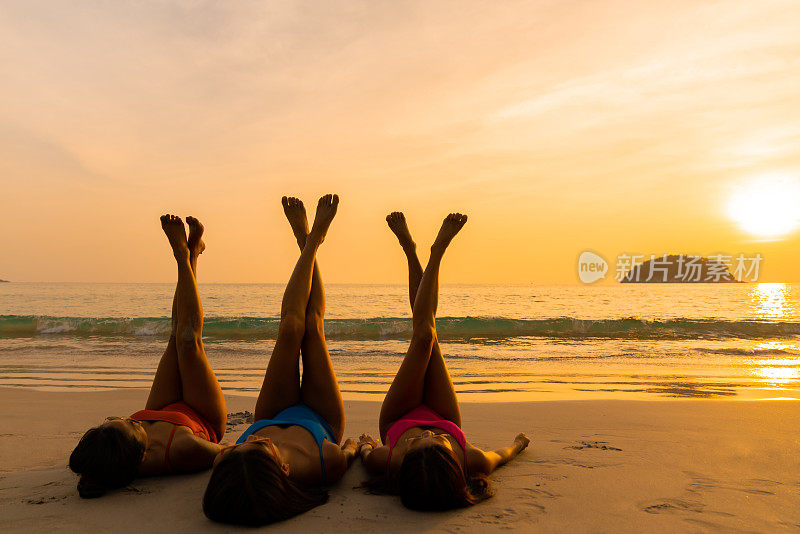 一群亚洲女性朋友躺在沙滩上，在夏日的夕阳下一起聊天。