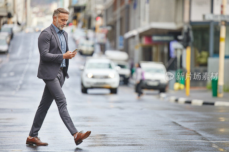一名英俊的商人一边使用智能手机，一边在城市中穿行