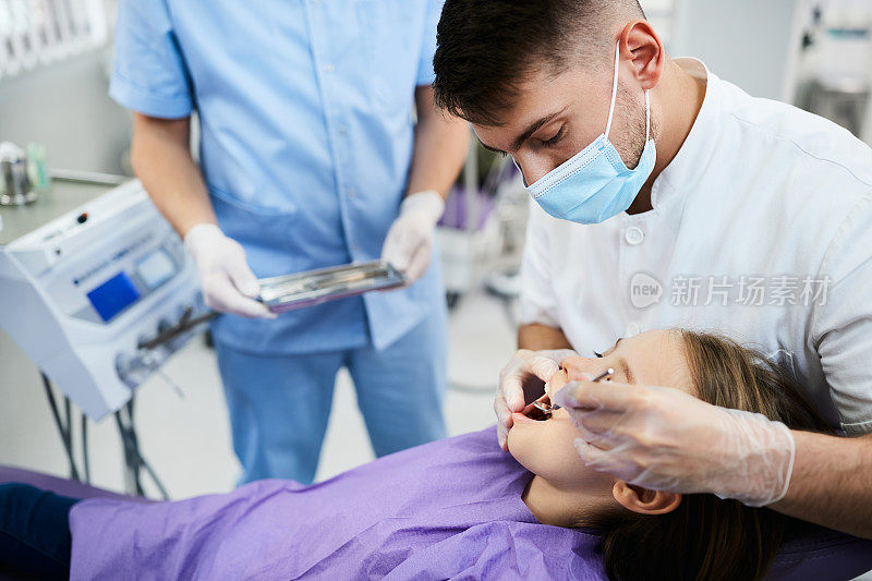 男牙医在牙科诊所检查小女孩的牙齿。