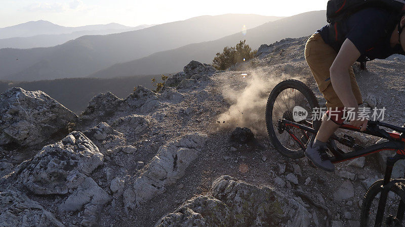 山地自行车手从岩石和尘土飞扬的斜坡上滑下