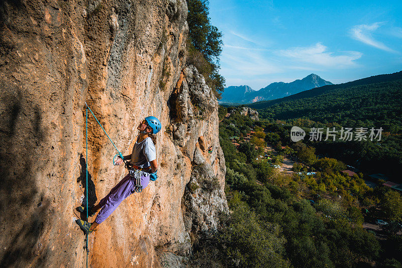 攀登者攀爬郁郁葱葱的山谷上陡峭的岩壁