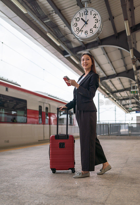 年轻美丽的亚洲女商人聊天在她的手机检查最新的旅行时间和护照信息，而在通勤列车站台等待火车