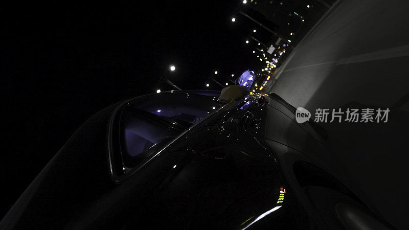 快速的黑色汽车行驶在城市的夜间道路上，从车轮上看，时间流逝。镜头。现代车辆行驶在繁忙的城市傍晚，自驾游概念。