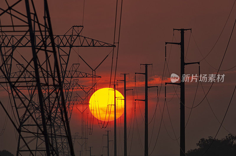 炎炎夏日，太阳落在一排高压输电塔和电线杆后面